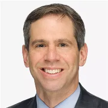 Smiling man in a suit with short hair against a plain background.