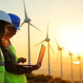 people - 2 workers looking at laptop in front of windmills at sunset