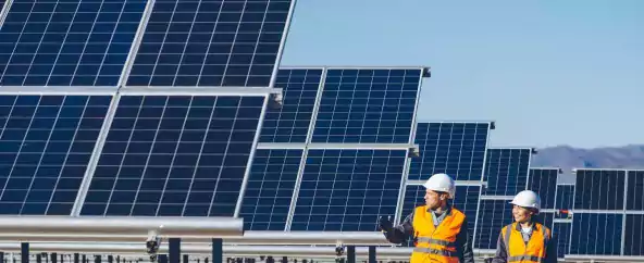 tech - man and woman workers in hard hats walking by solar panels