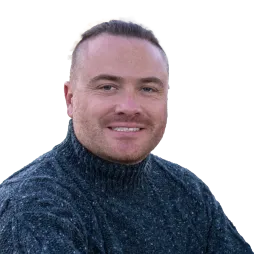 A professional headshot of Paul Makarewicz, smiling warmly. He is wearing a textured gray turtleneck sweater and is set against a plain background.