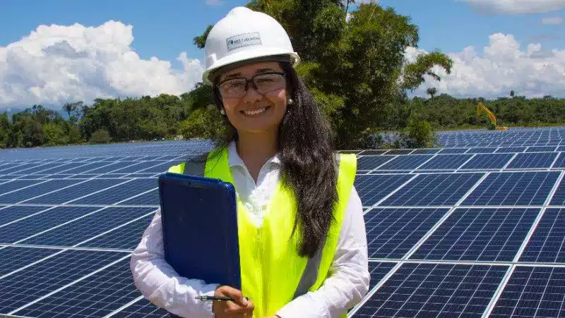 Woman standing by solar panel, wearing safety gear