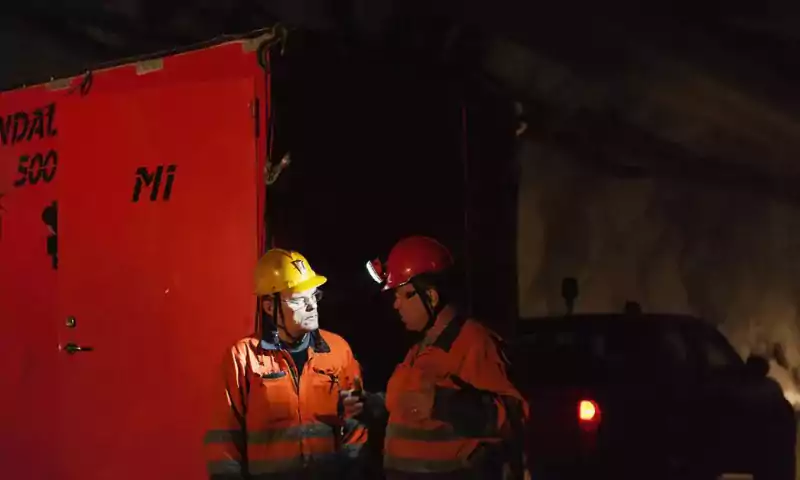 Two workers at night with headlamps talking in front of a battery storage unit
