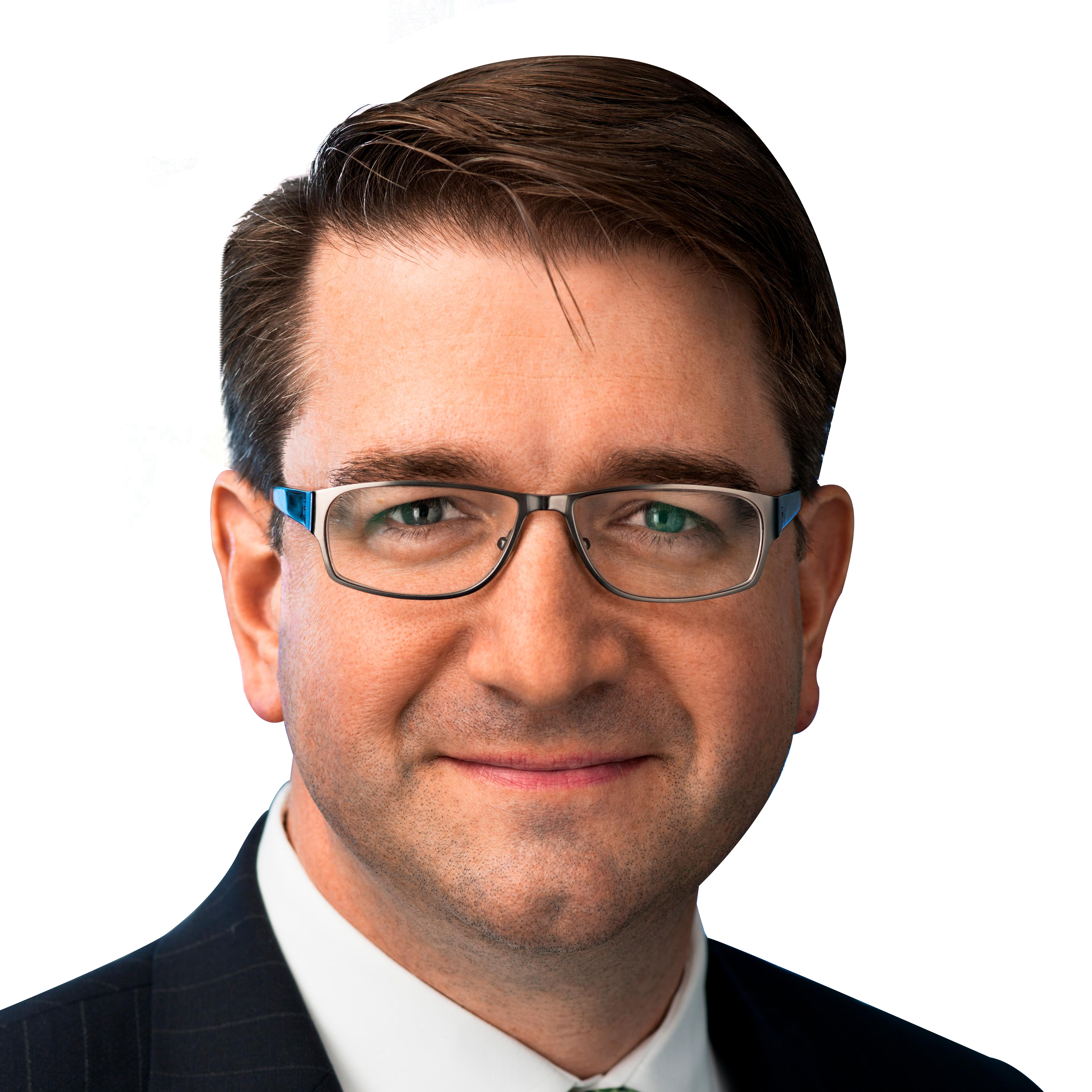 Portrait of a man with glasses, wearing a suit and tie, smiling against a black background.