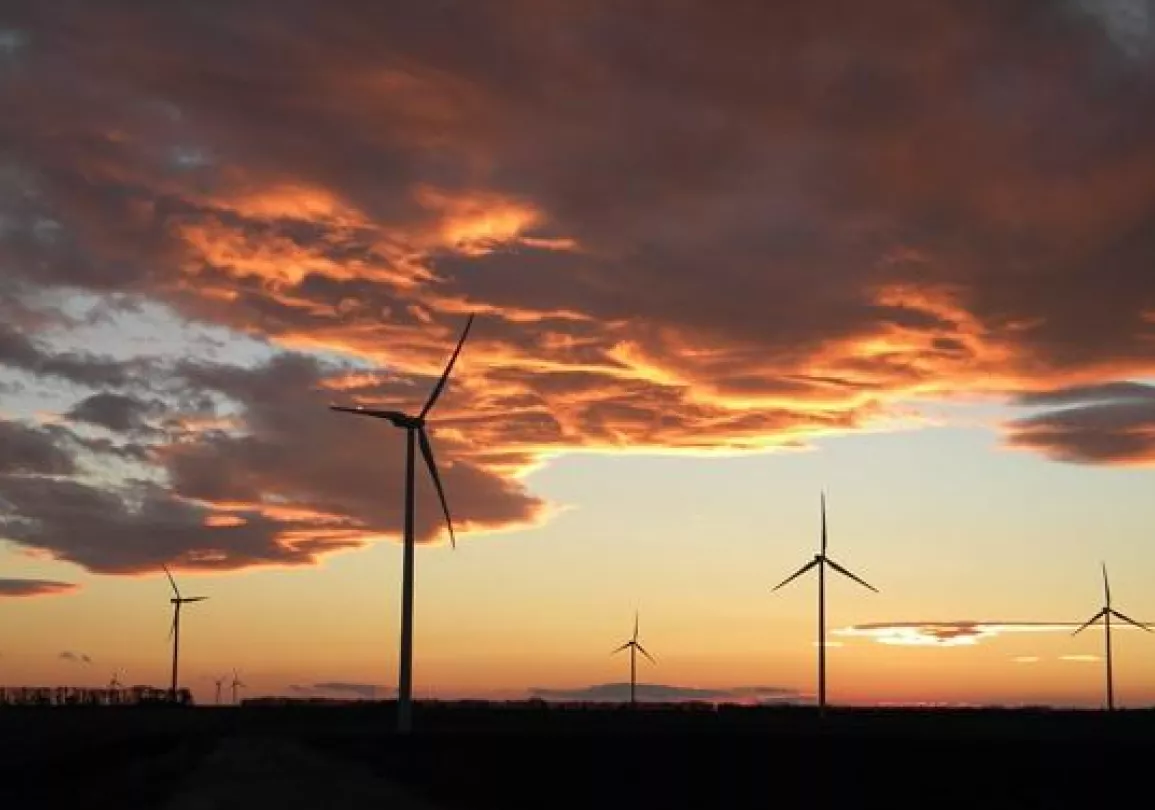 Wind turbines silhouetted against a vibrant sunset sky with orange and purple clouds.