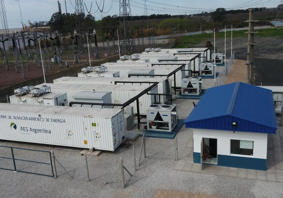 Aerial view of an energy storage facility with multiple white container units labeled 'AES Argentina' and a small building with a blue roof.