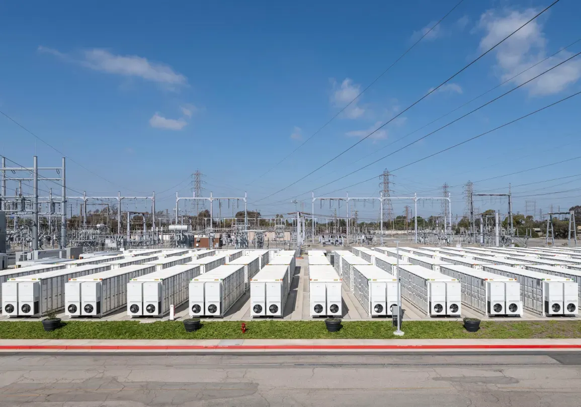 Rows of white industrial battery energy storage system containers in a solar field with electrical transmission towers.