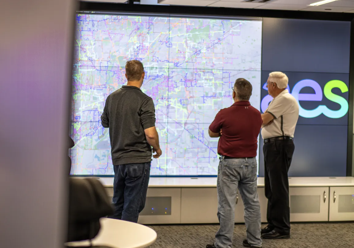 Employees reviewing a large digital map display showing electric grid infrastructure and network data.