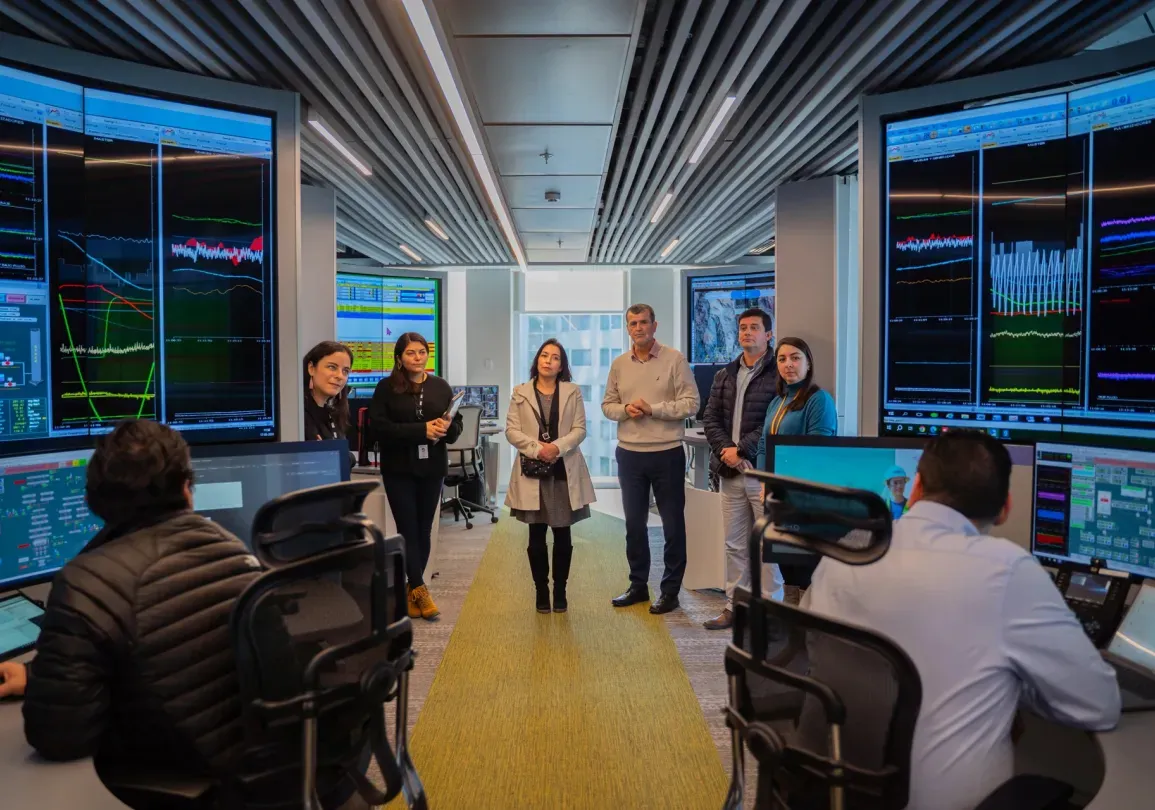 A group of professionals standing in a modern office monitoring center filled with large digital data displays.