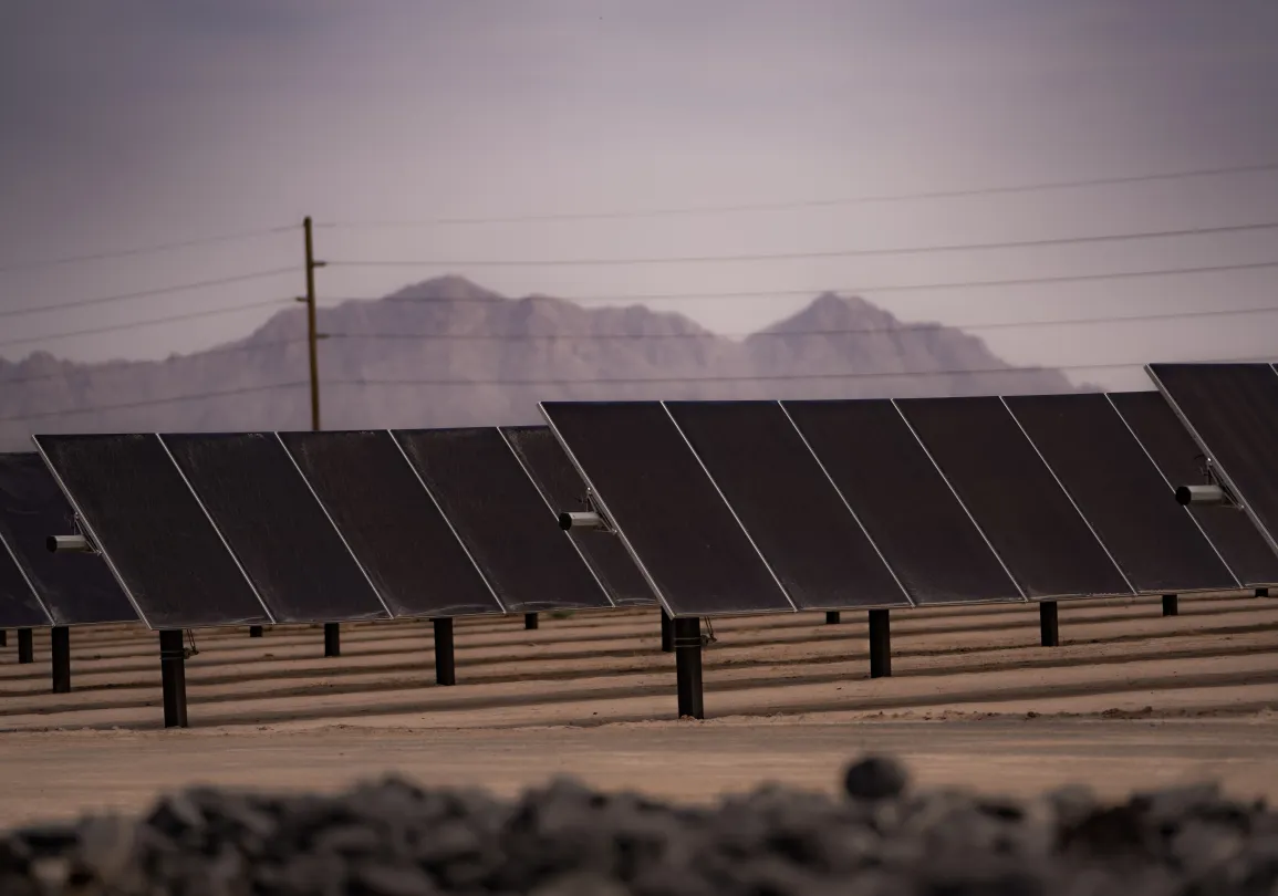 Rows of solar panels at a utility-scale solar energy facility with mountains in the background.