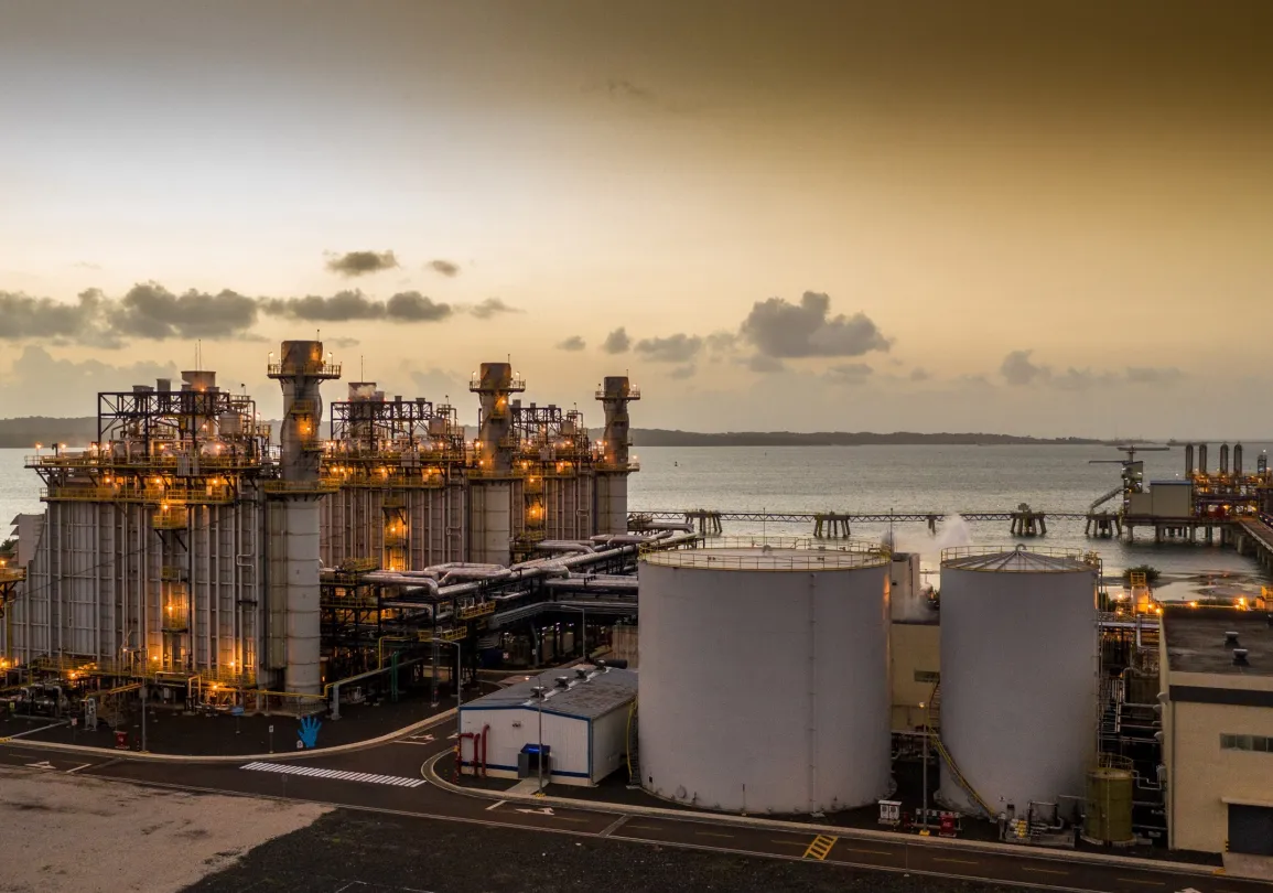 Industrial power plant with storage tanks and a pier at sunset along the coastline.