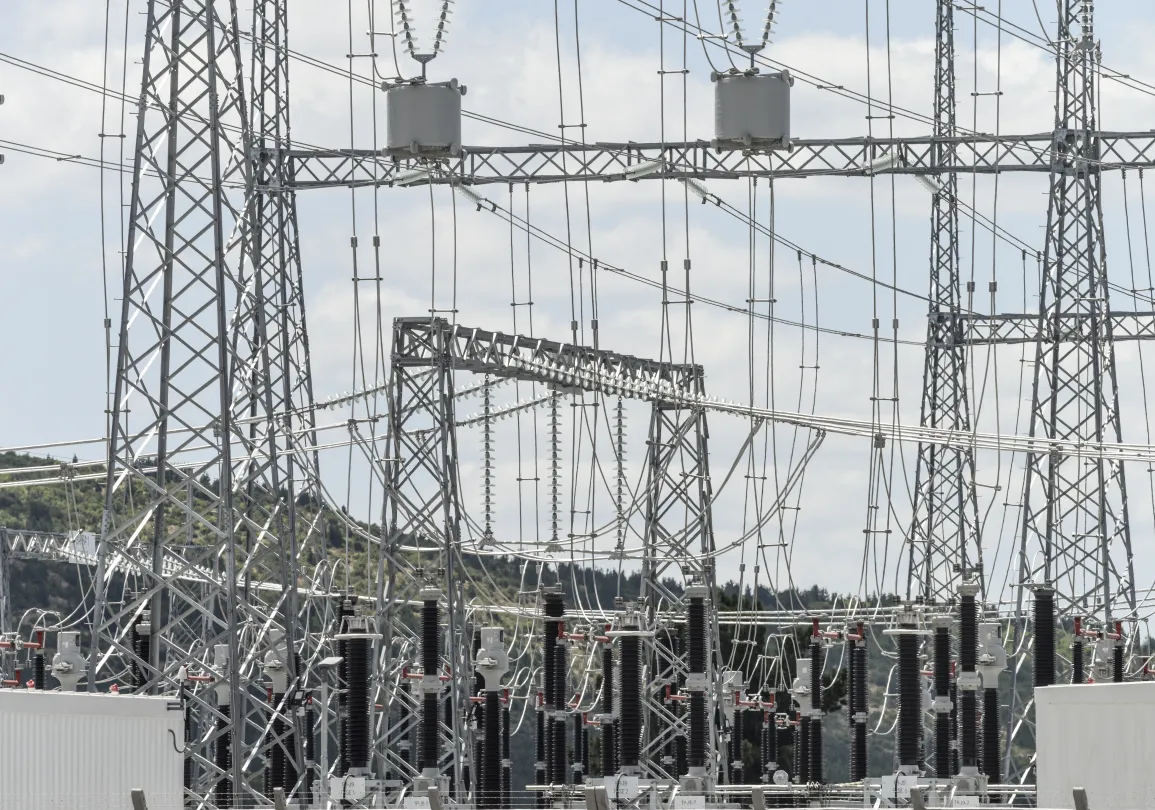 Complex electrical substation with steel lattice towers, transmission lines, and large ceramic insulators.
