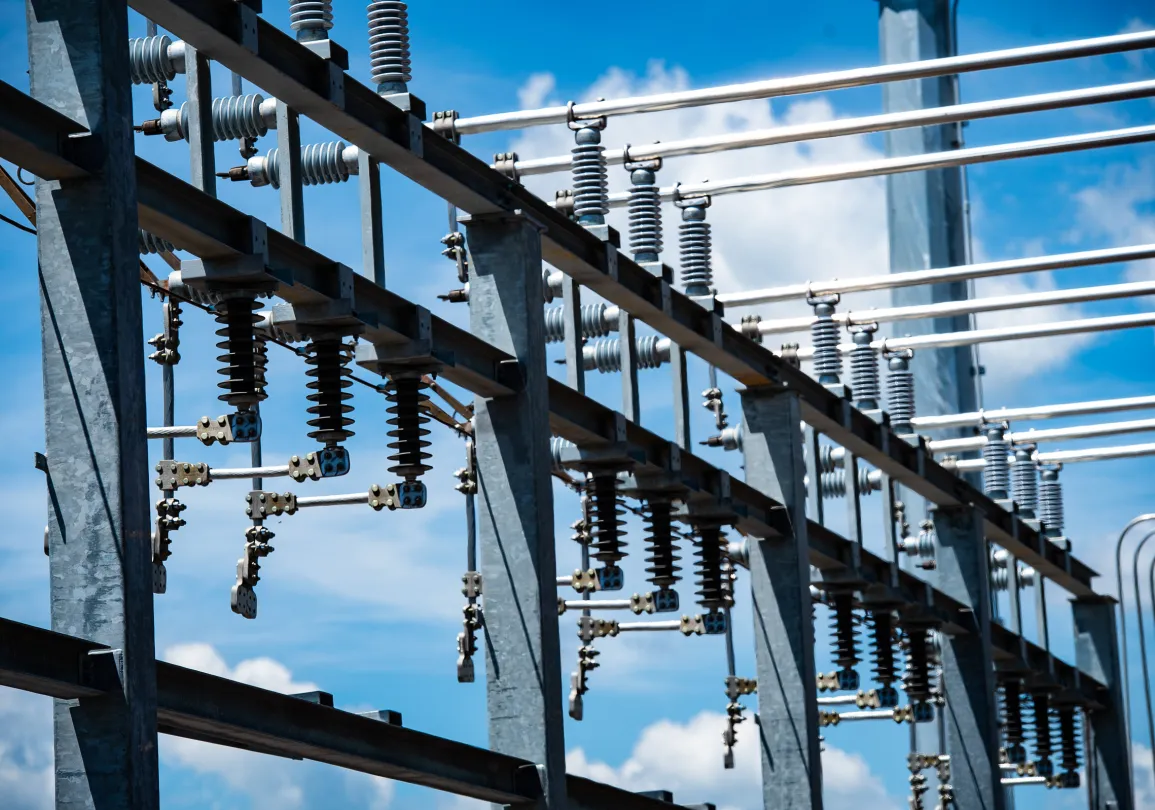 Close-up of high-voltage electrical substation equipment with porcelain insulators mounted on steel structures against a sky.