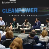 Panel discussion at Clean Power event with five speakers seated on stage, engaging with an audience. The backdrop displays the words 'Clean Power Leading the Charge'.