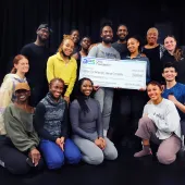 A group of people smiling and posing with a large ceremonial check from the AES Ohio Foundation, made out to the Dayton Contemporary Dance Company for $55,000, dated February 22, 2023. The group is standing and kneeling in front of a dark background.