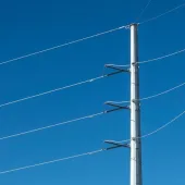A tall metal utility pole with four power lines against a clear blue sky.