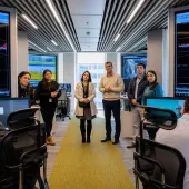 A group of professionals standing in a modern control center filled with monitors displaying data graphs.
