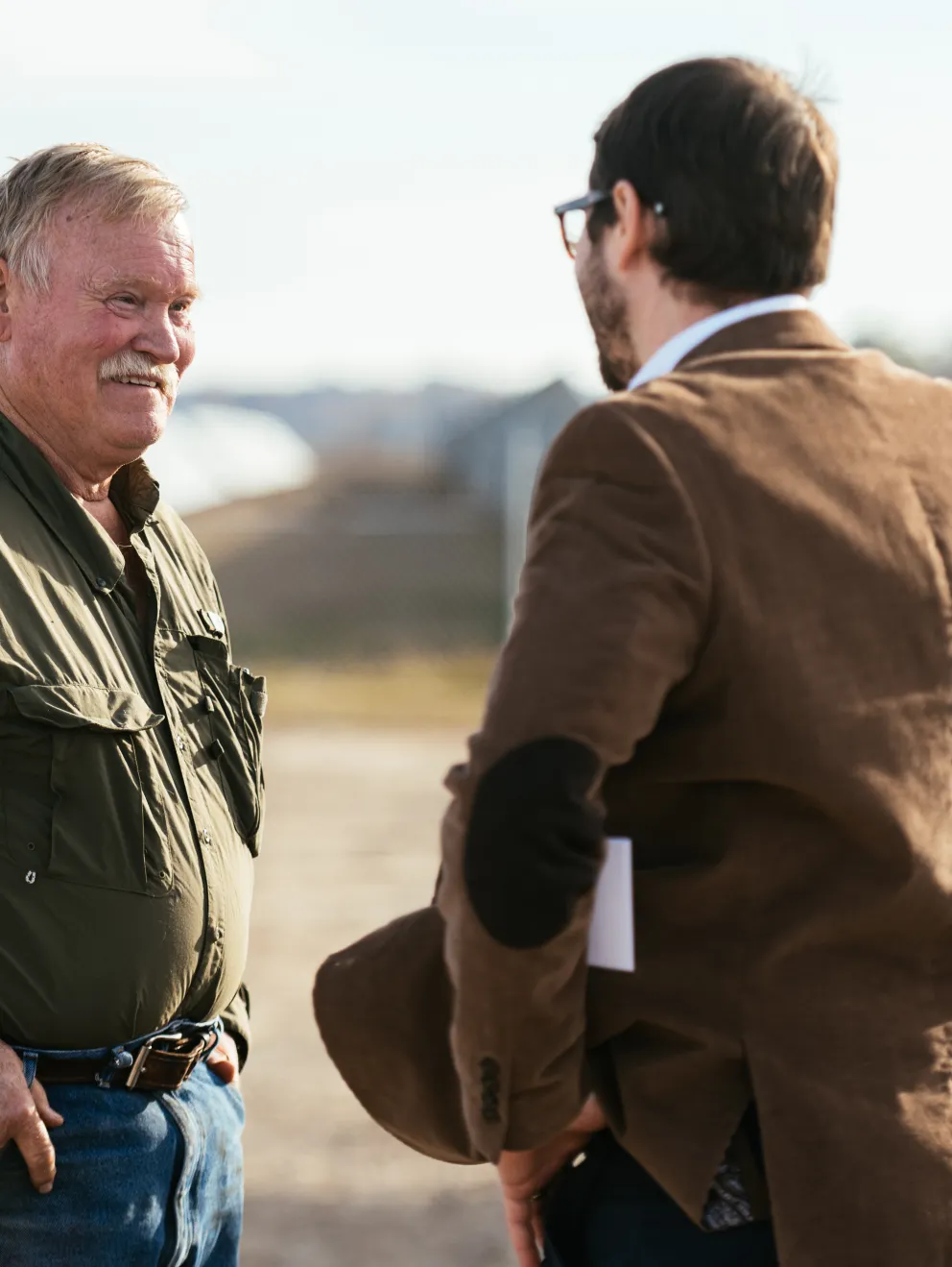 Two professionals having a discussion at an AES renewable energy site, with solar panels and construction equipment in the background.