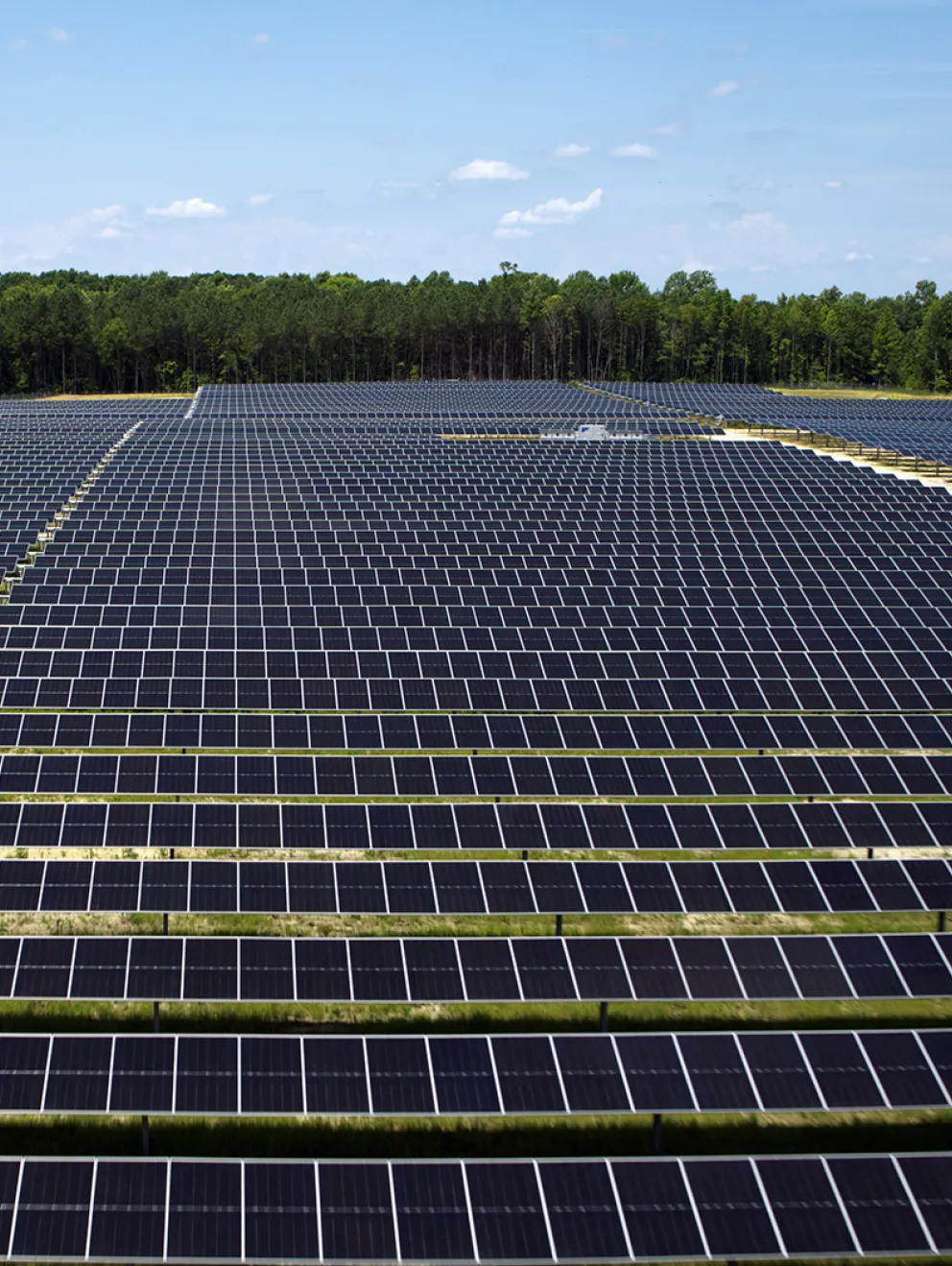 Aerial view of a large utility-scale solar farm with rows of photovoltaic panels generating clean renewable energy under a clear blue sky.