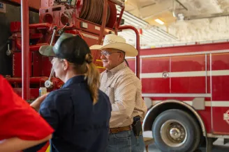 A man in a cowboy hat and a woman in a cap stand near a red fire truck inside a garage.