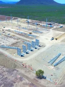 Aerial view of a large construction site with steel structures and equipment, surrounded by dry land and greenery in the distance.