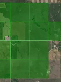 Aerial view of farmland with large green fields divided by grid lines, surrounded by patches of brown and tan land.