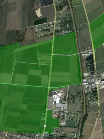 Aerial view of a rural area with large green fields, roads, and scattered buildings. The fields are outlined in bright green, indicating boundaries.