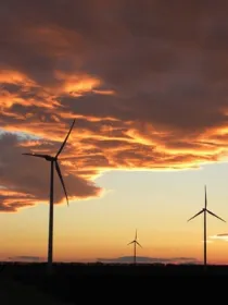 Silhouetted wind turbines under a dramatic sunset sky with orange and gray clouds.