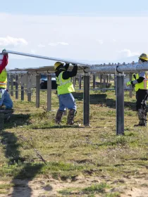 Construction workers in a grassy field placing a solar panel on top of a racking system.
