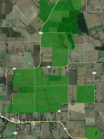 Aerial view of farmland with outlined green fields and intersecting roads, displaying a patchwork of cultivated land.