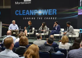 Panel discussion at Clean Power event with five speakers seated on stage, engaging with an audience. The backdrop displays the words 'Clean Power Leading the Charge'.
