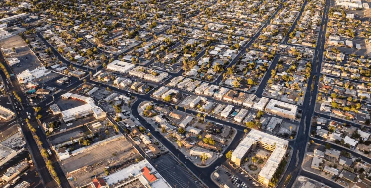Aerial view of a sprawling urban landscape with a grid pattern of streets and densely packed buildings, interspersed with trees and green spaces.