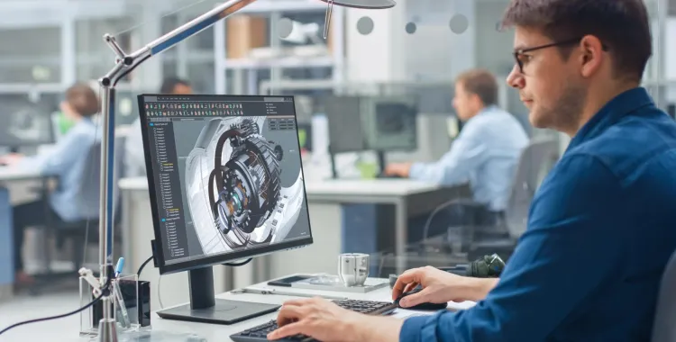 Engineer working at a desk in a modern office, using computer-aided design (CAD) software to create a 3D model of a mechanical part on a large monitor. Other professionals are working at desks in the background, creating a collaborative workspace environment.