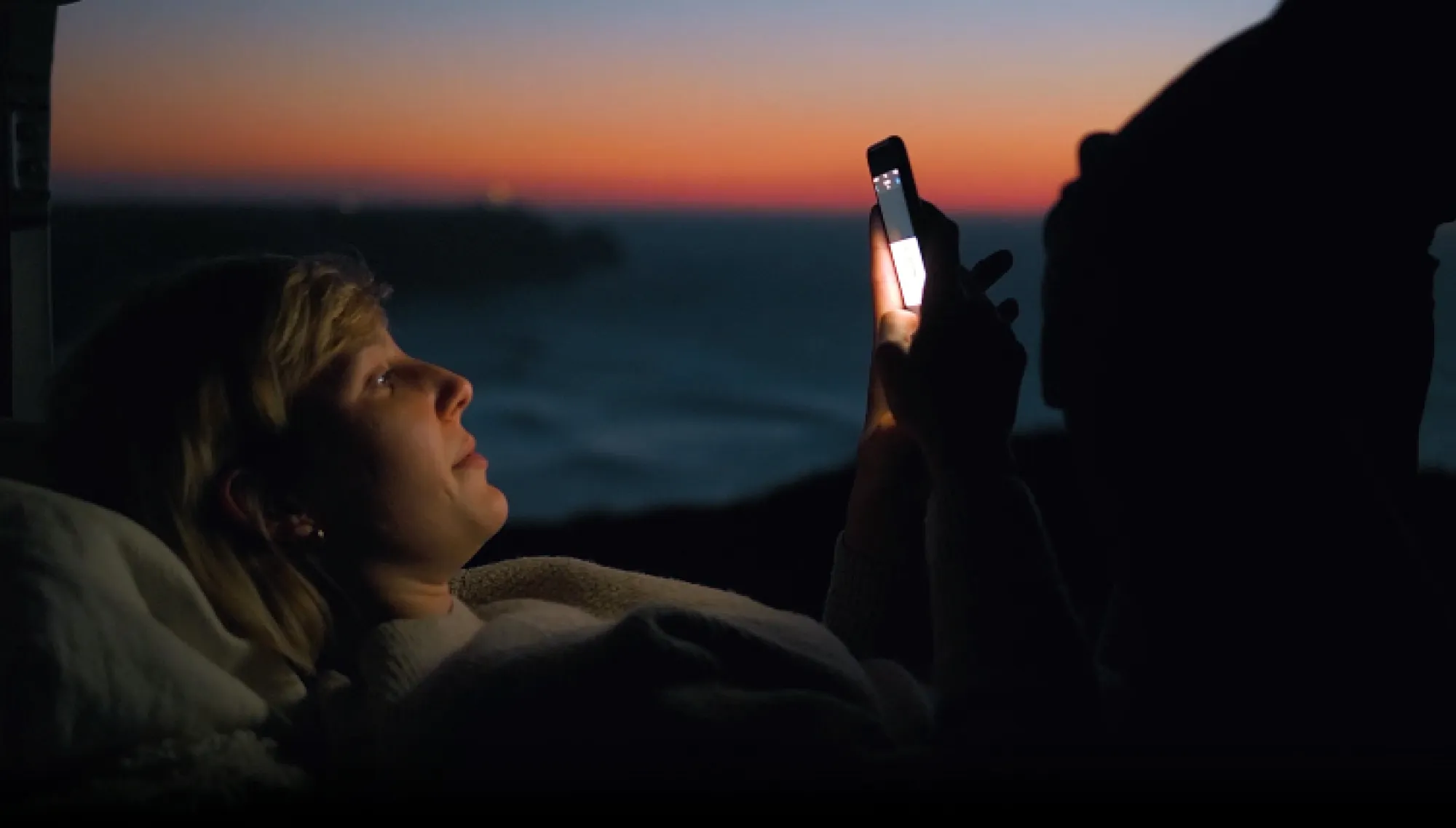 Smartphone displaying an energy savings app in a home setting overlooking a coastal landscape at sunset.
