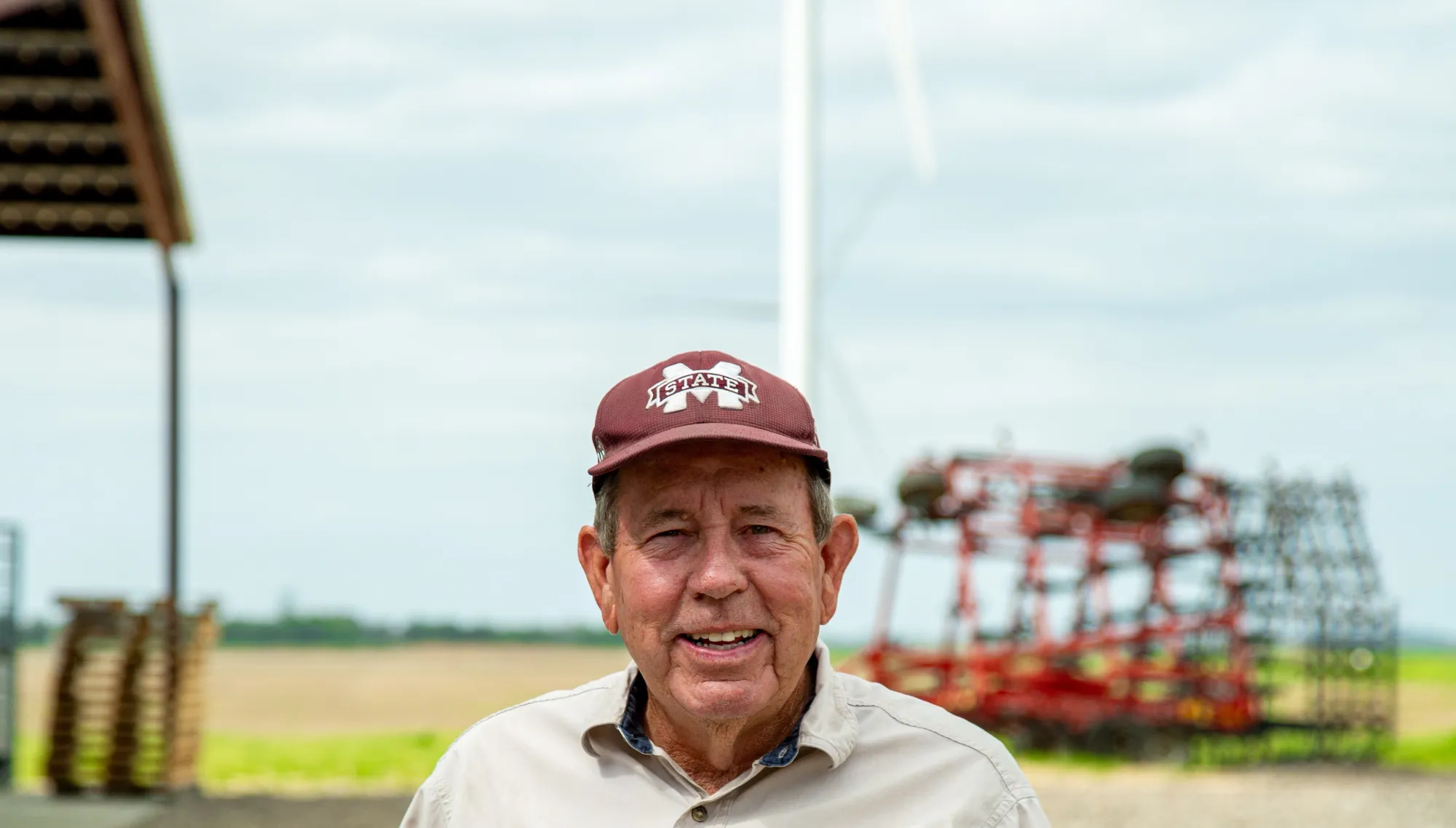 Man standing in front of wind turbine and farm equipment