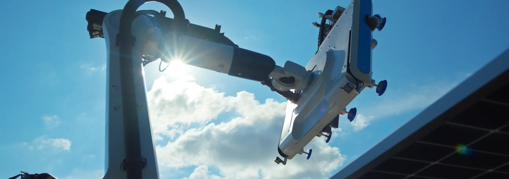 A robotic arm extends towards the sky with the sun shining brightly behind it, partially obscured by clouds. The arm is positioned near a solar panel, indicating a technological setting.