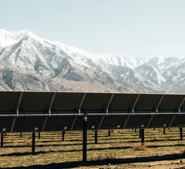Solar panels in a field with snow-capped mountains in the background under a clear sky.