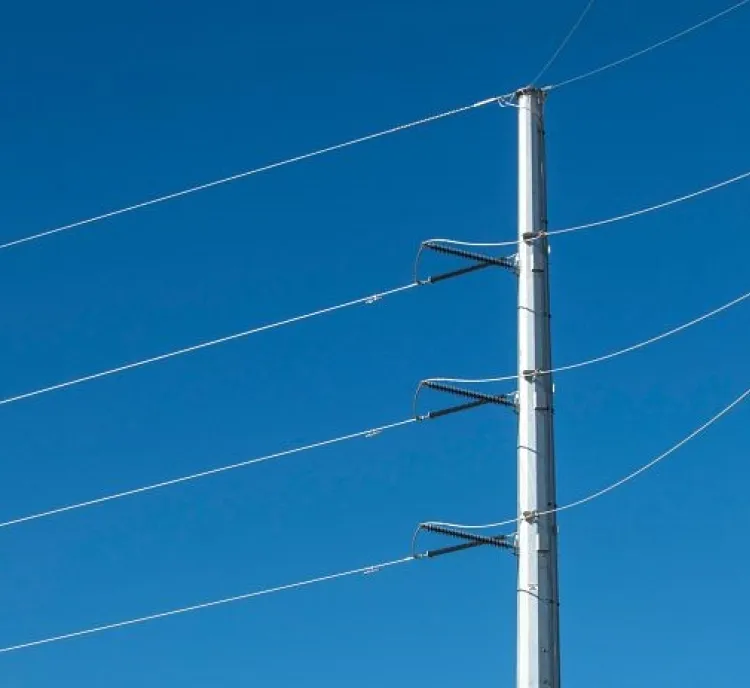 A tall metal utility pole with four power lines against a clear blue sky.