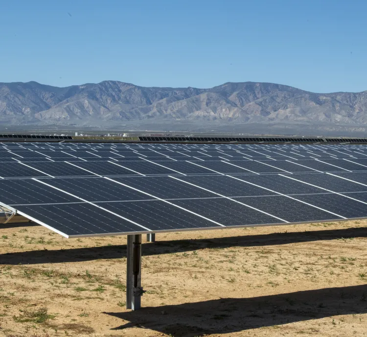 Rows of solar panels in a desert landscape with mountains in the background under a clear blue sky.