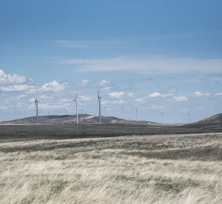 A landscape with several wind turbines on a grassy plain under a blue sky with scattered clouds.