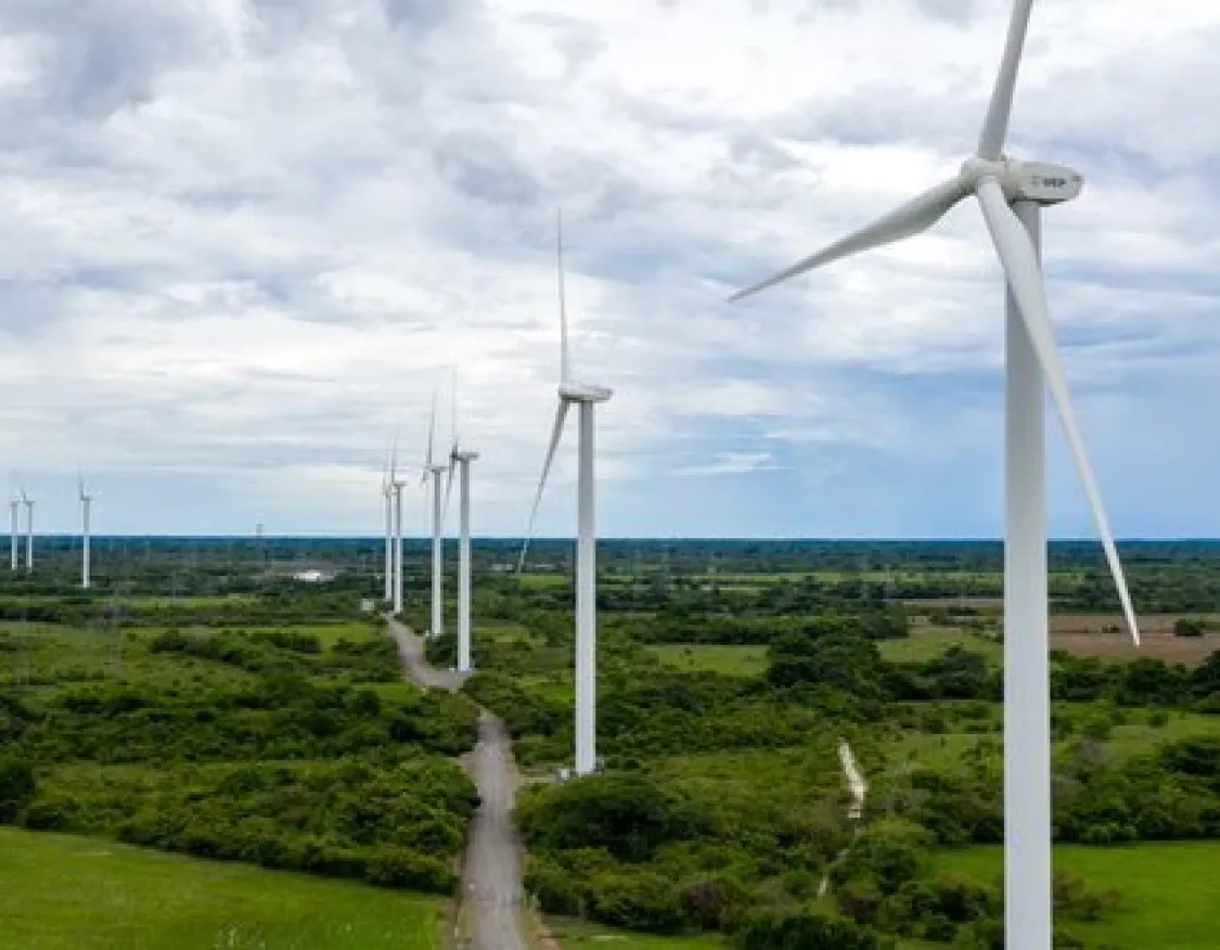 A row of wind turbines in a green landscape under a cloudy sky, generating renewable energy.