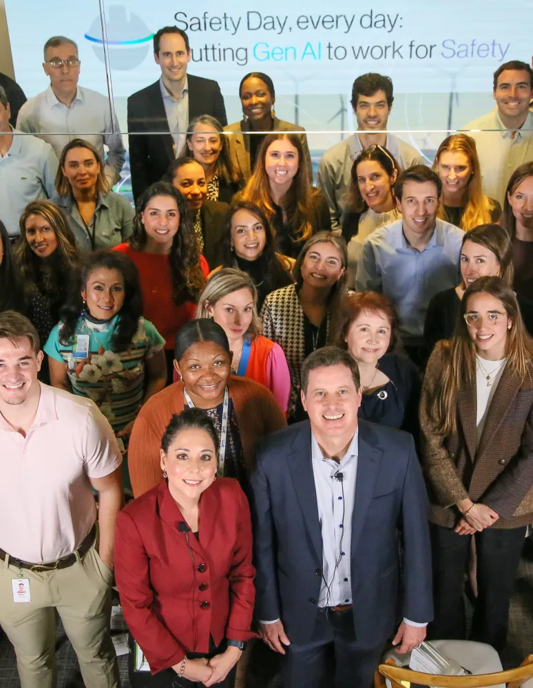 A large group of diverse individuals smiling and standing together in a room with a banner in the background reading "Safety Day, every day".