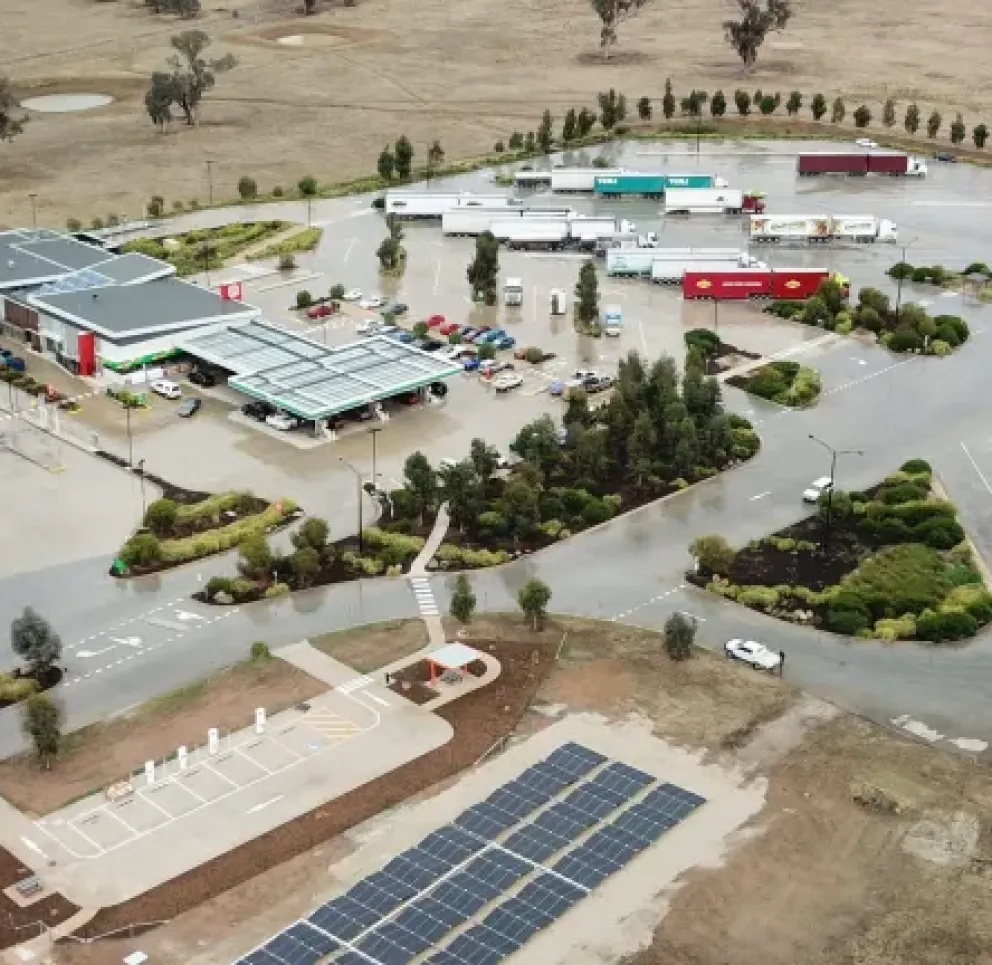 Aerial view of a roadside service station with multiple buildings, parked trucks, and a solar panel installation in a rural area.
