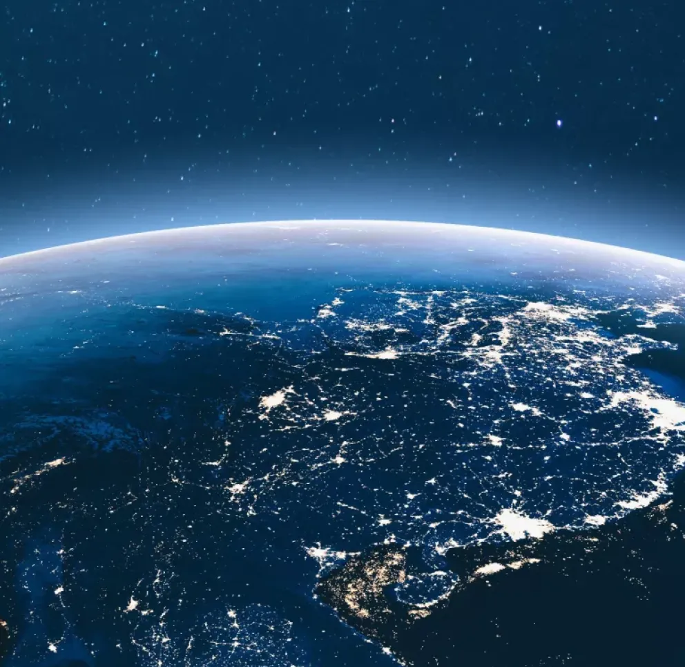 A view of Earth from space at night, showing illuminated city lights across continents under a starry sky.