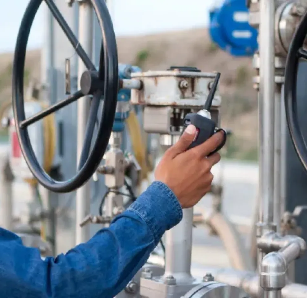 A worker in a hard hat and safety glasses operates a control valve at an industrial site.
