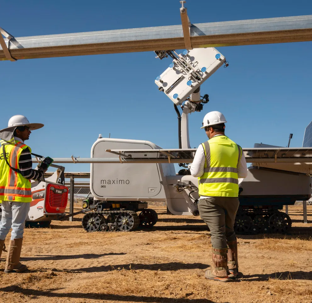 Three workers in safety gear operate a solar panel cleaning robot in a solar farm under a clear blue sky.