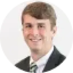 A man in a suit with a green striped tie smiling against a plain background.