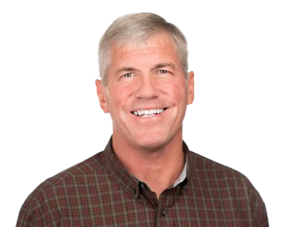 Smiling middle-aged man with short gray hair wearing a red and green plaid button-up shirt, standing against a plain white background.