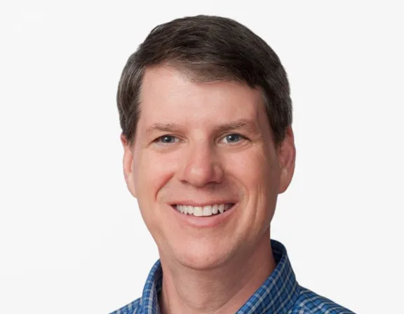 Portrait of a smiling man wearing a blue checkered button-down shirt against a plain white background.