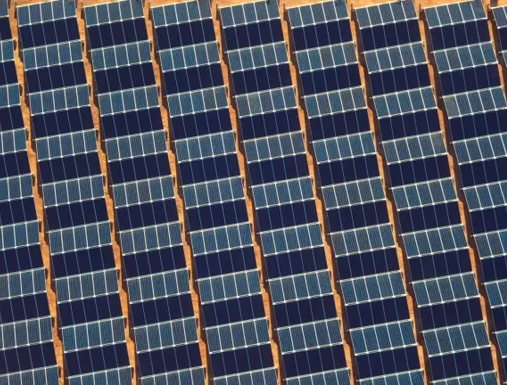 Aerial view of a large solar panel farm with rows of solar panels on a sandy terrain.