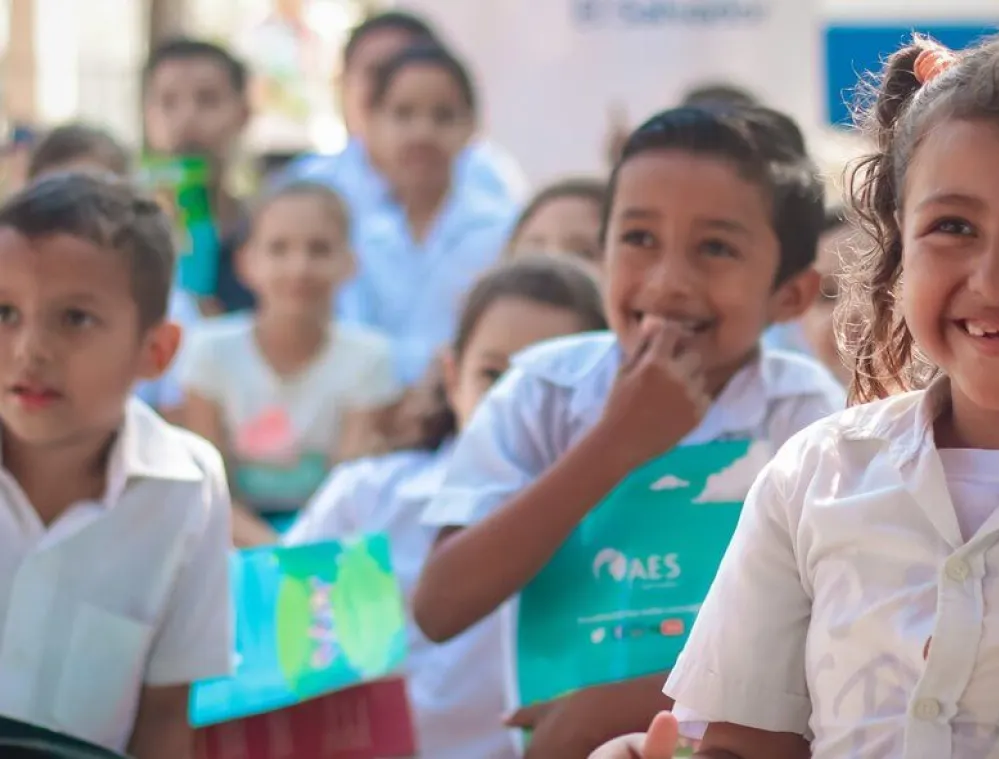 Group of young children in school uniforms smiling and holding colorful folders during an outdoor event.